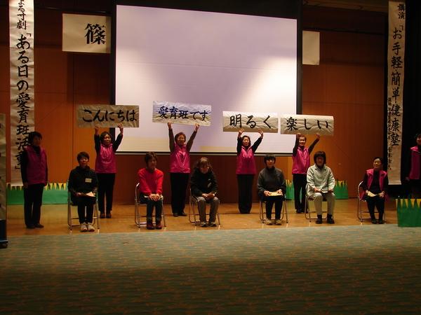 スクリーンの前で椅子に座った女性や文字の書いた紙で言葉を表現している写真